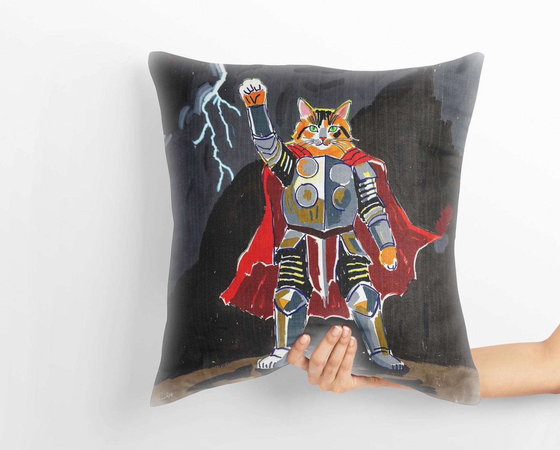 A hand holds a custom medieval pet portrait pillow featuring a tabby cat dressed as Thor, wielding a hammer and standing in a stormy landscape. The whimsical art captures the heroic spirit of the pet.