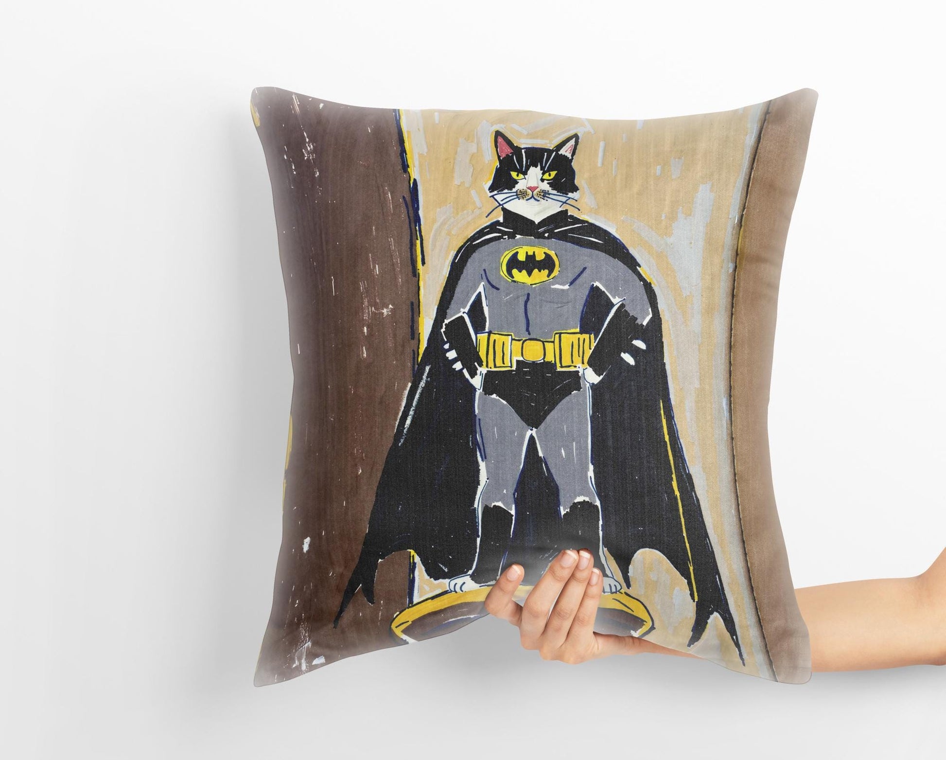 A hand holds a custom medieval pet portrait pillow featuring a black and white cat dressed as Batman, standing on a pedestal. The whimsical art captures the playful spirit of the pet.