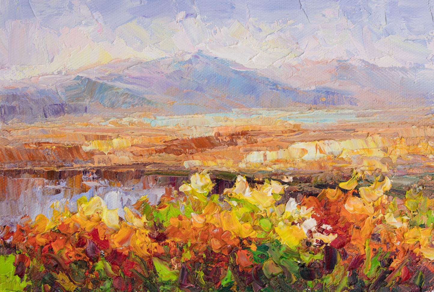 Unframed oil painting of a desert landscape at sunset with vibrant yellow and orange flowers in the foreground, layered mountains in the distance, and textured brushwork on canvas