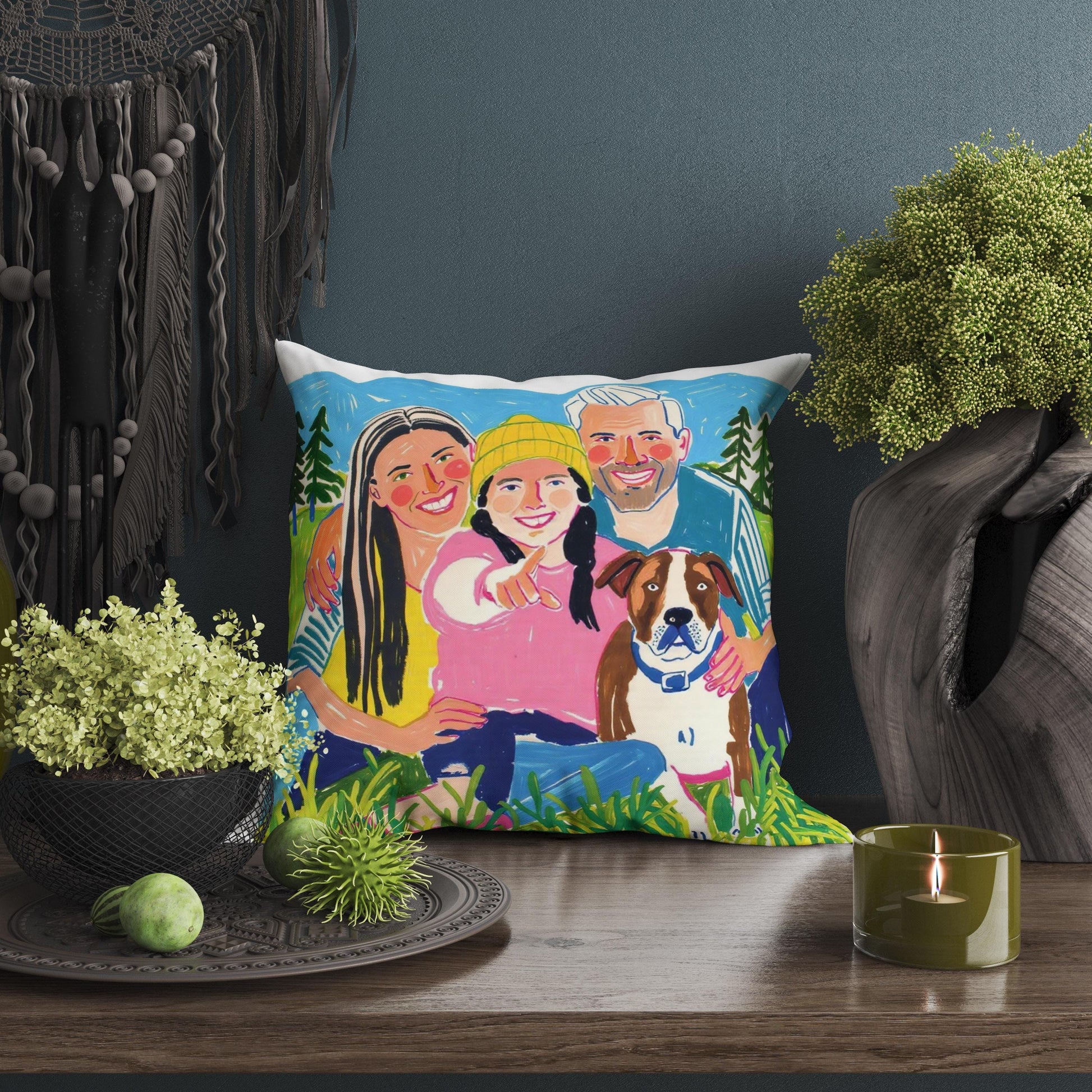 Custom pet portrait pillow featuring a family with their dog in a park, displayed on a wooden table with decorative items. The whimsical art captures the special bond between family and pet.