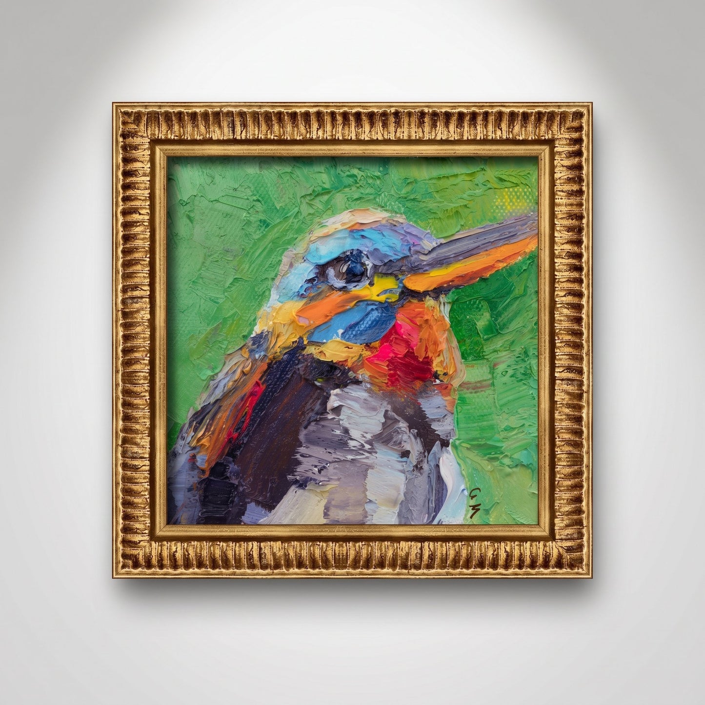 A vividly painted kingfisher with bold blue, red, and green hues hangs in an ornate gold frame on a softly lit white wall.