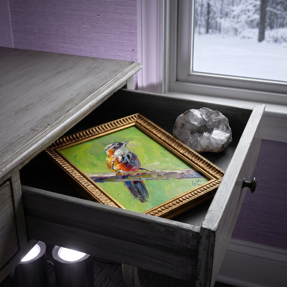 A colorful bird painting on canvas rests inside a weathered wooden drawer beside a geode, bathed in soft winter light from a nearby window.