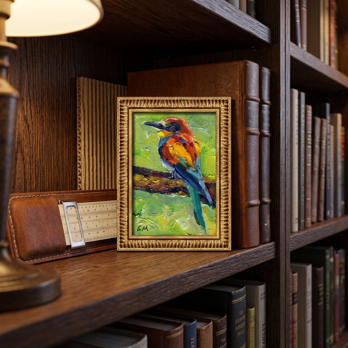 A vividly painted bird perched on a branch, rendered in bold orange, blue, and green hues, sits framed on a wooden bookshelf beside a vintage ruler and leather case.