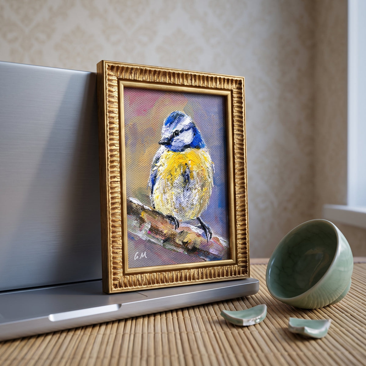 A vivid oil painting of a blue and yellow bird perched on a branch, framed in ornate gold, sits beside a broken teacup on a bamboo mat in a sunlit kitchen nook.