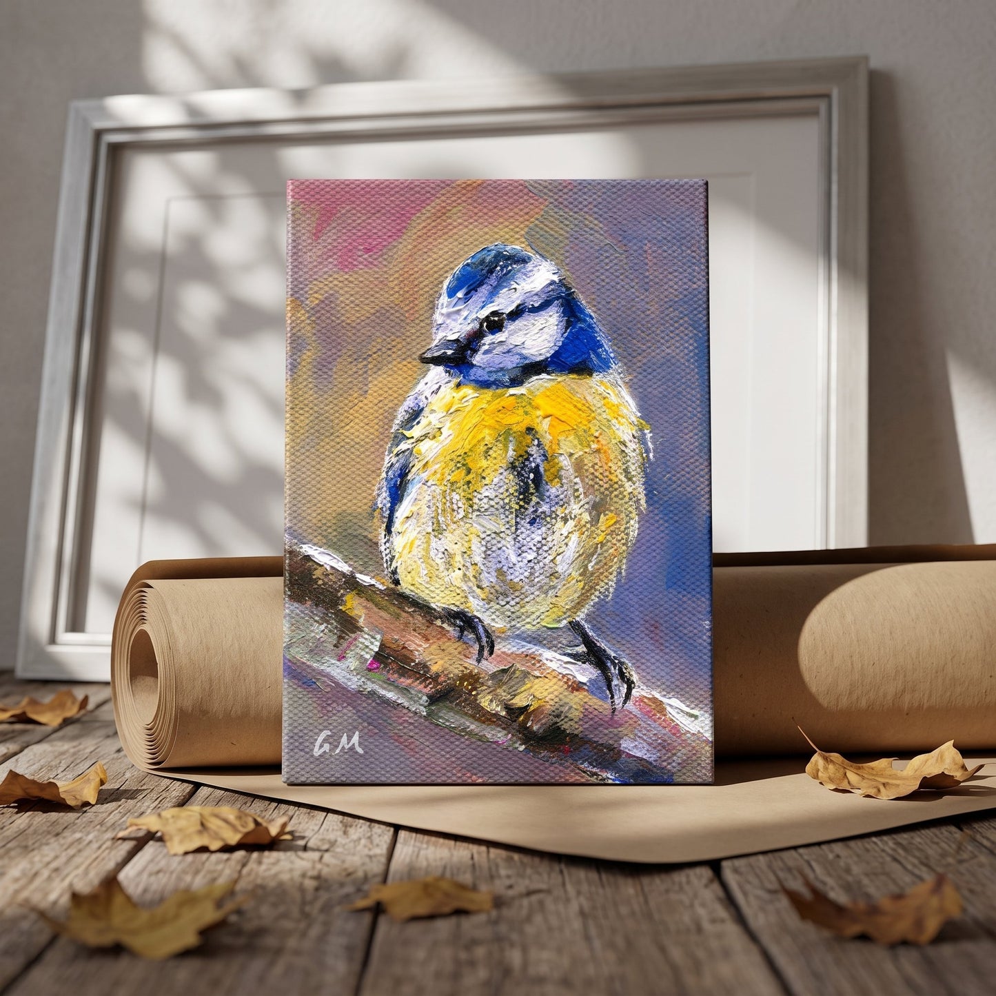 A vivid blue and yellow bird painting rests on a wooden floor beside rolled paper, bathed in dappled sunlight, unframed canvas.
