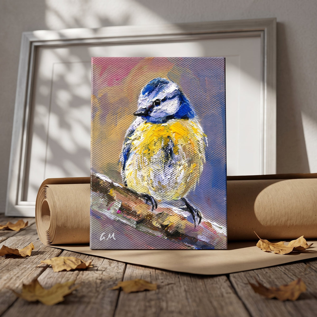 A vivid blue and yellow bird painting rests on a wooden floor beside rolled paper, bathed in dappled sunlight, unframed canvas.