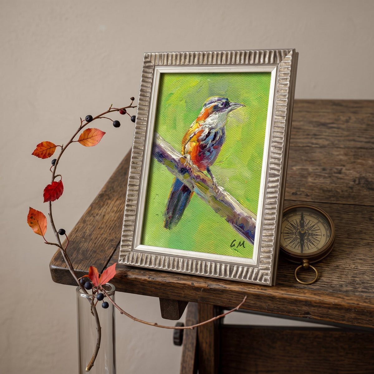 A vivid oil painting of a colorful bird perched on a branch, set in a textured silver frame atop a rustic wooden desk beside autumn leaves and a vintage compass.