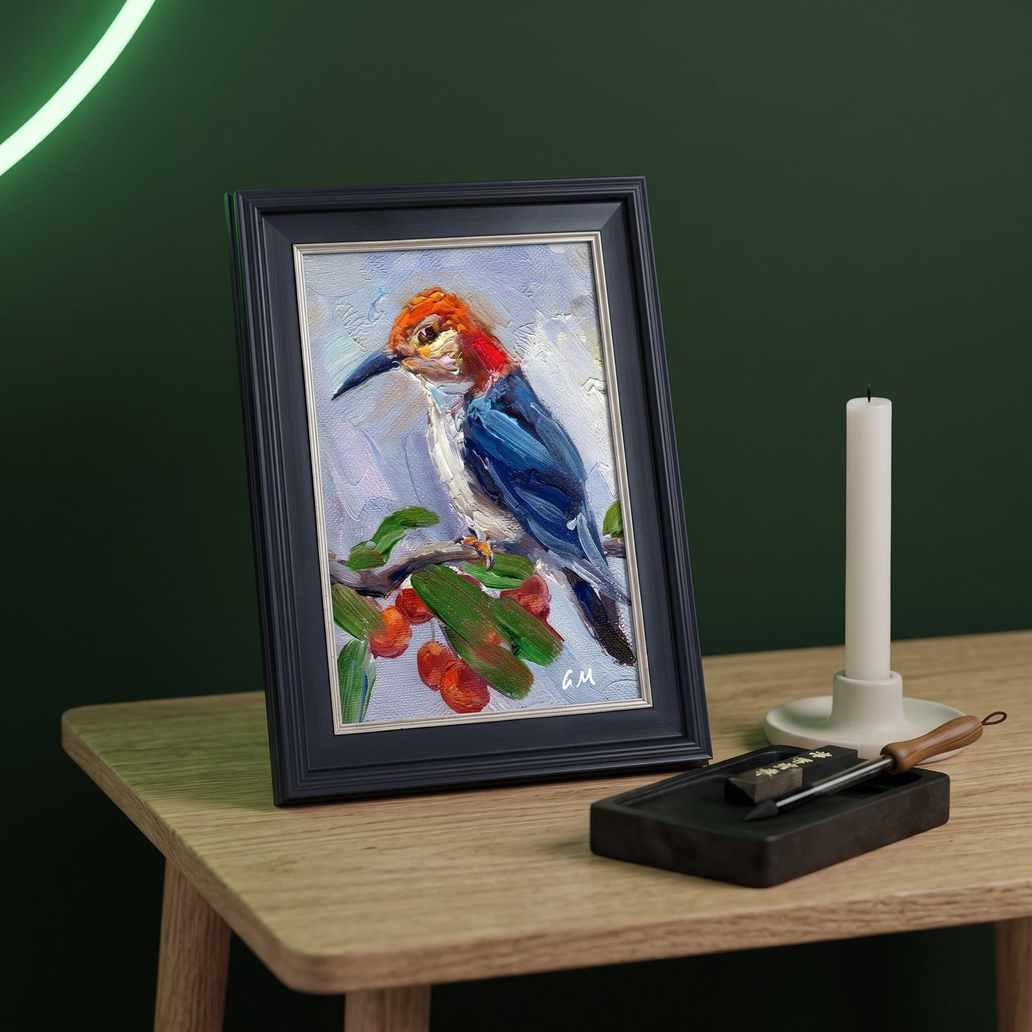 A vividly painted woodpecker with blue feathers and orange crown perches on a branch in a framed canvas, set on a wooden desk beside a candle and inkstone.