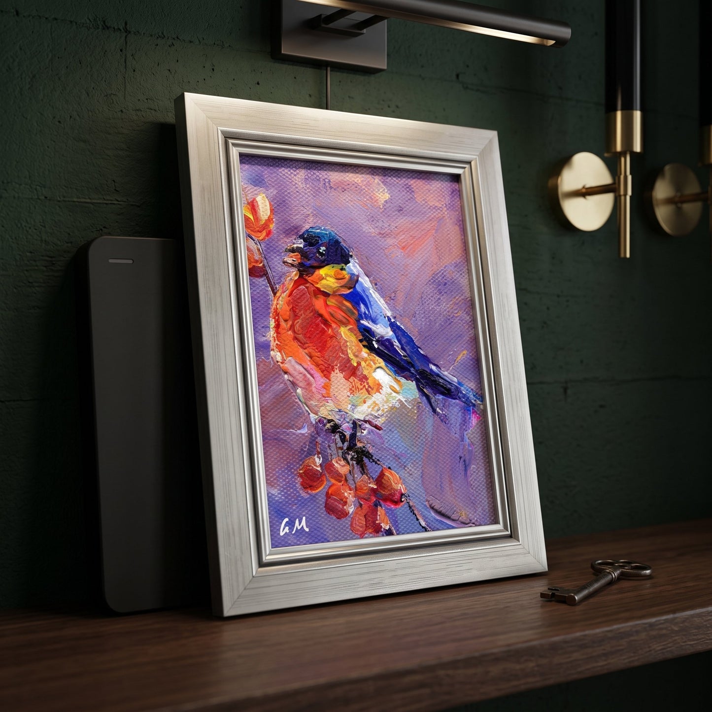 A vividly painted robin in fiery reds and deep blues rests on a branch of berries, displayed unframed on a dark wood console beside a vintage key and modern sconce.