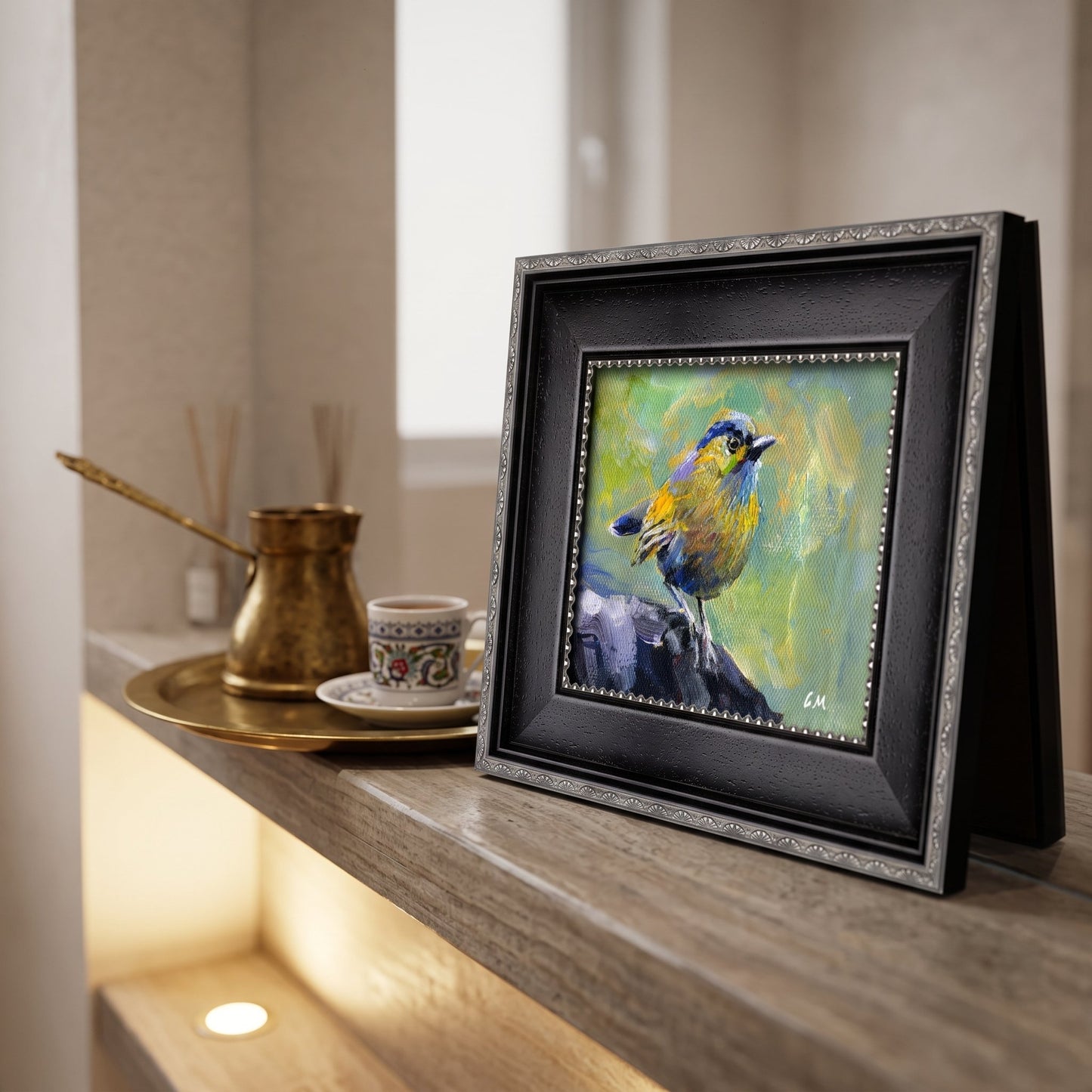 A vividly painted bird in green, yellow, and blue rests on a rock in a framed canvas, displayed on a wooden shelf beside a brass coffee set.