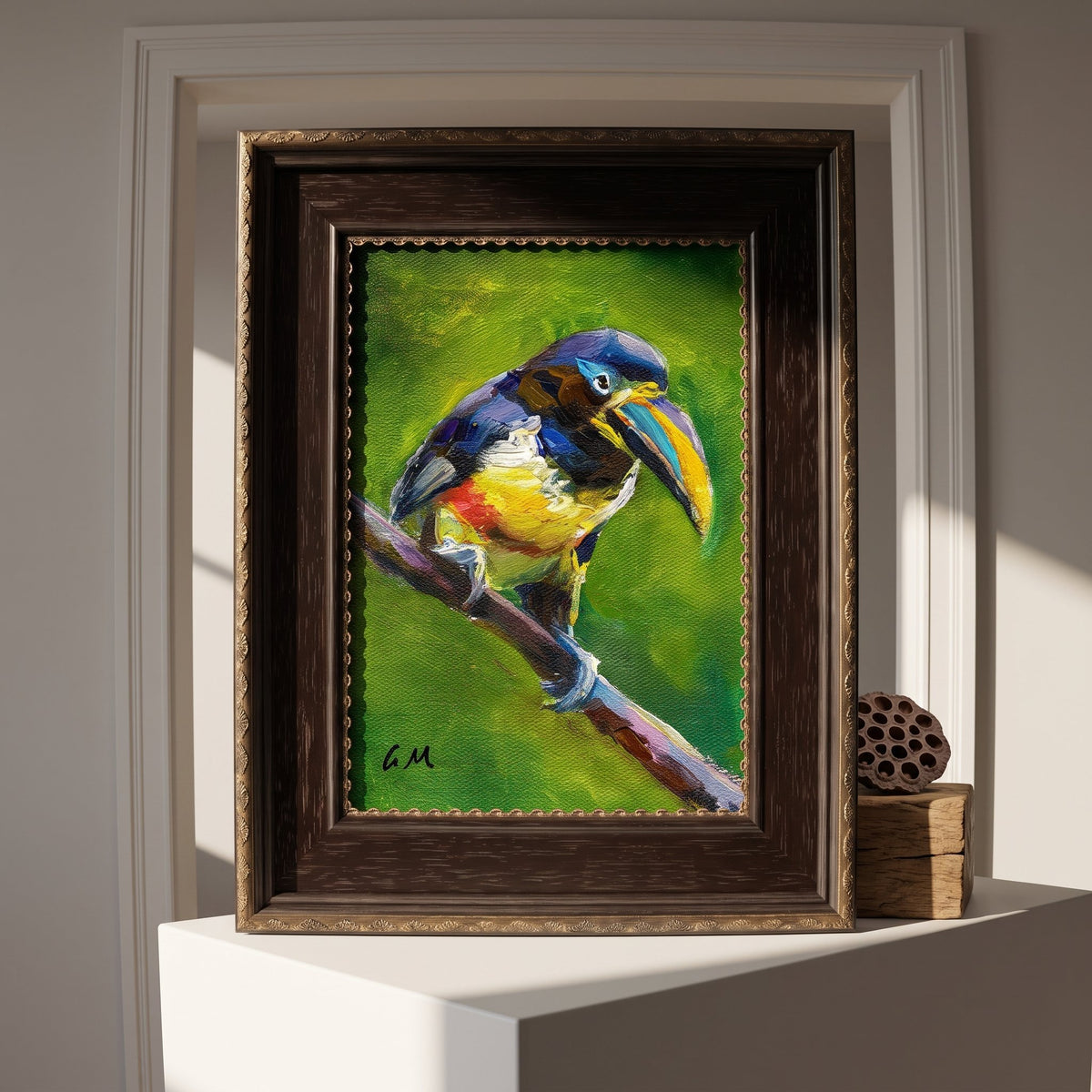 A vividly painted toucan perched on a branch, rendered in bold greens, blues, and yellows, sits framed in dark wood atop a white pedestal in a sunlit entryway.